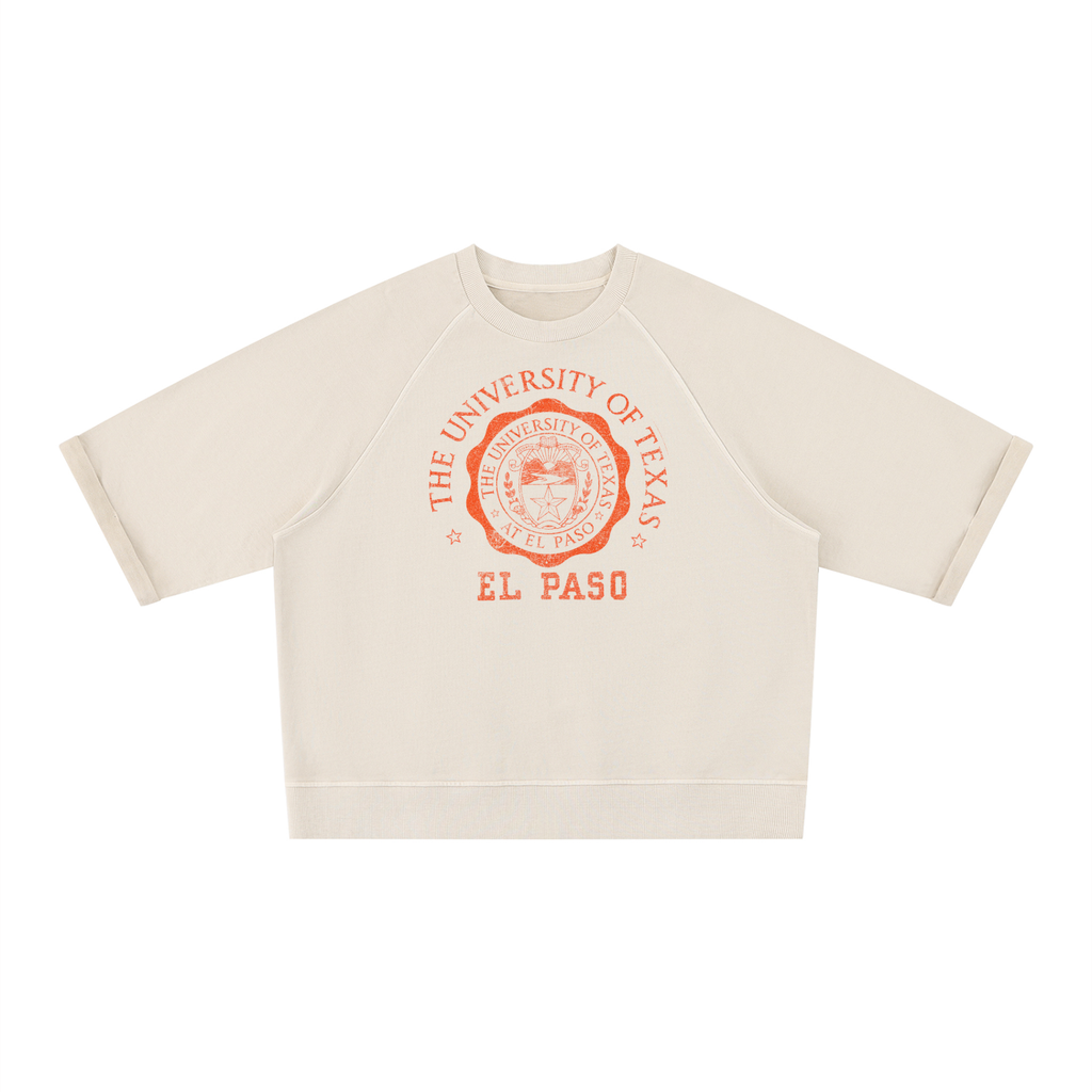 An off-white cropped short-sleeve sweatshirt featuring a red-orange graphic print of the University of Texas El Paso seal on the chest, displayed flat against a solid white background.